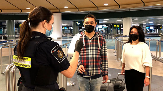 Photo montrant une agente des services frontaliers du Canada qui interroge deux voyageurs dans un aéroport
