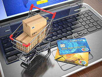 Photo of a laptop computer, credit cards, and a miniature shopping cart with boxes