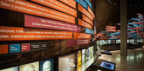 Photo of a room showing interactive digital stations, monitors of people speaking, and bilingual posters on the wall about human rights