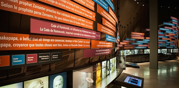 Photo d’une salle abritant des postes numériques interactifs, des écrans montrant des personnes qui parlent et des affiches bilingues sur le mur au sujet des droits de la personne